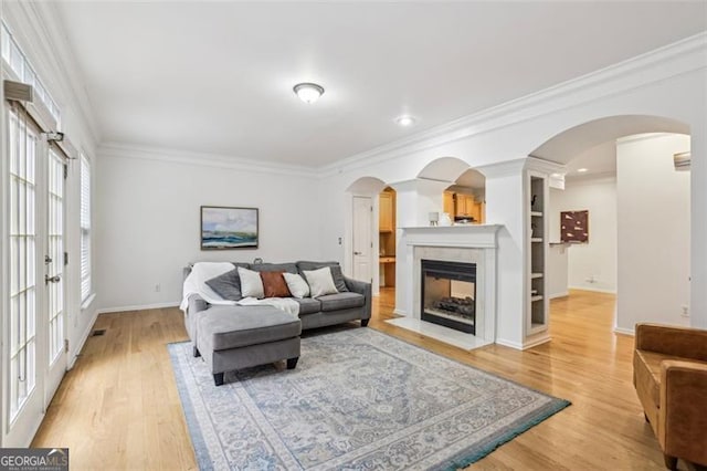 living room featuring a fireplace with flush hearth, crown molding, baseboards, light wood-type flooring, and french doors