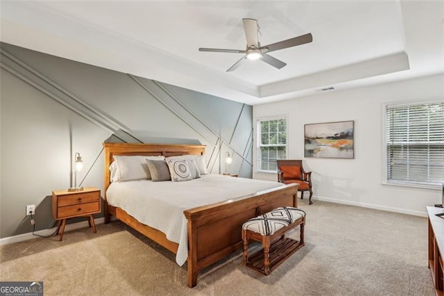 bedroom with baseboards, light colored carpet, visible vents, and a raised ceiling