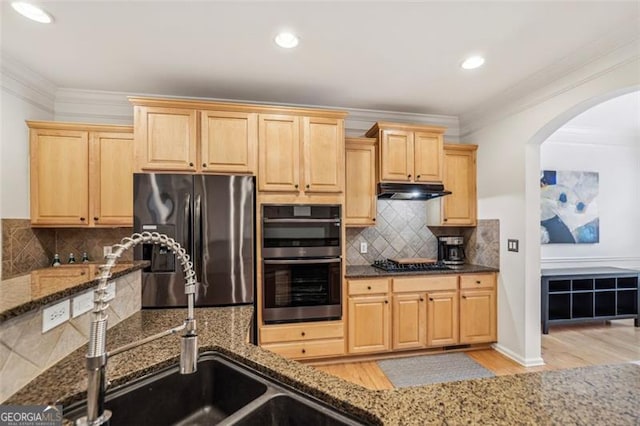 kitchen with arched walkways, dark stone counters, light brown cabinetry, and appliances with stainless steel finishes