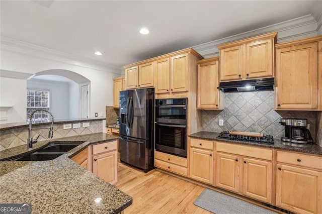 kitchen featuring under cabinet range hood, light brown cabinetry, arched walkways, black appliances, and a sink