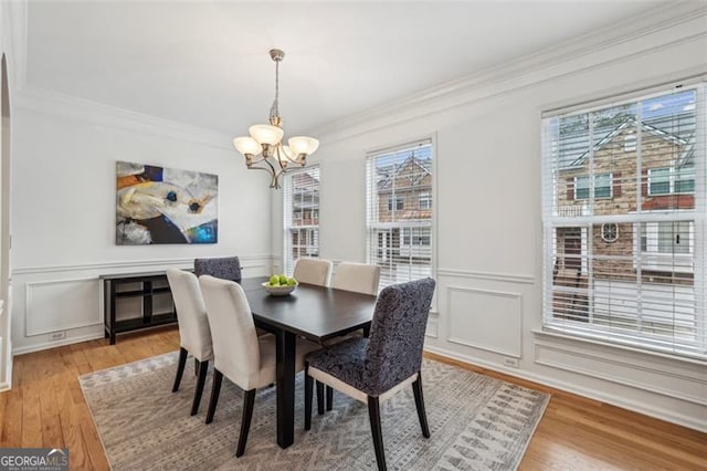 dining space with a decorative wall, a chandelier, crown molding, and light wood finished floors