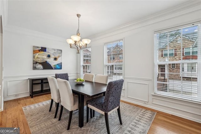 dining space featuring a decorative wall, ornamental molding, light wood-type flooring, and a chandelier