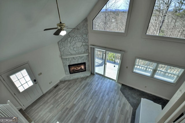 unfurnished living room featuring a ceiling fan, wood finished floors, visible vents, high vaulted ceiling, and a stone fireplace