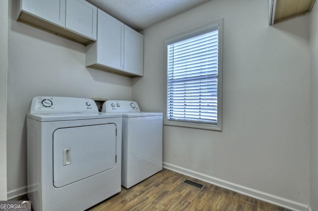 laundry area featuring washing machine and clothes dryer, visible vents, baseboards, wood finished floors, and cabinet space