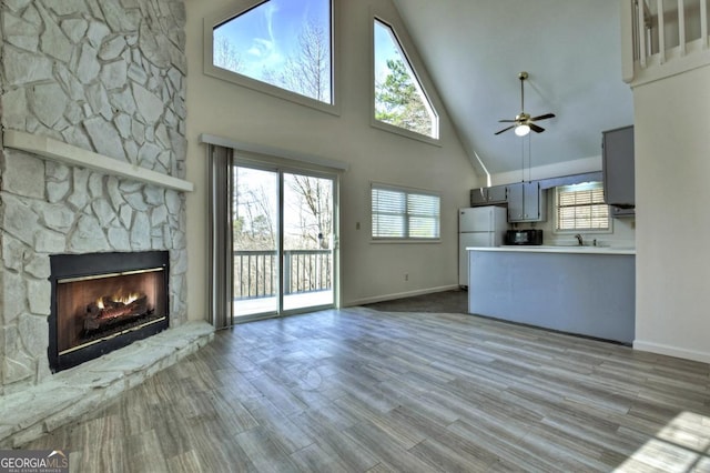 unfurnished living room featuring plenty of natural light, a fireplace, ceiling fan, and wood finished floors