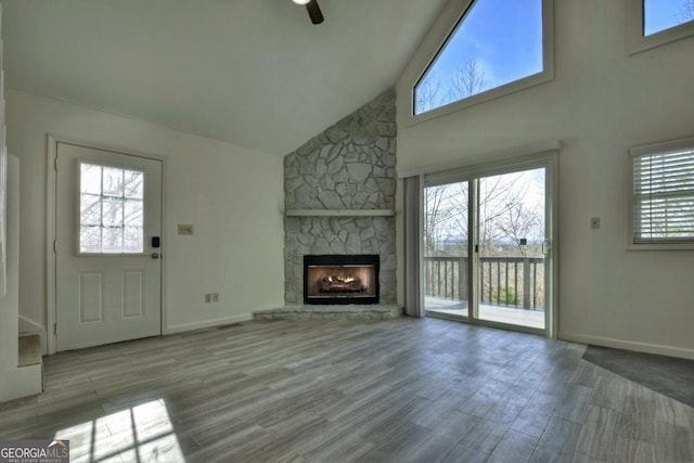 unfurnished living room with baseboards, high vaulted ceiling, a stone fireplace, and wood finished floors