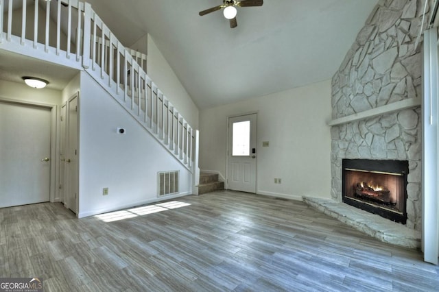 unfurnished living room with visible vents, ceiling fan, stairs, a stone fireplace, and wood finished floors