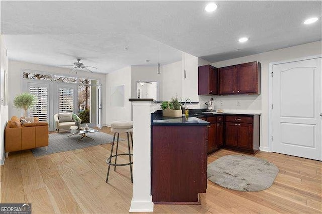 kitchen with open floor plan, light wood-type flooring, a peninsula, french doors, and a kitchen breakfast bar