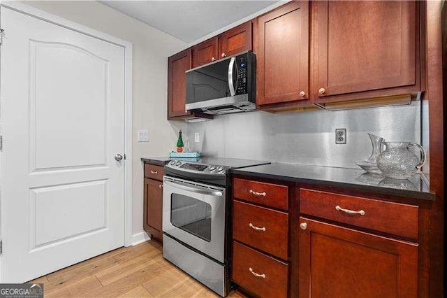 kitchen with dark countertops, backsplash, appliances with stainless steel finishes, and light wood-type flooring