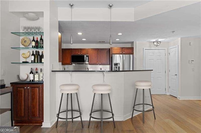 kitchen with dark countertops, appliances with stainless steel finishes, light wood-type flooring, and a kitchen breakfast bar