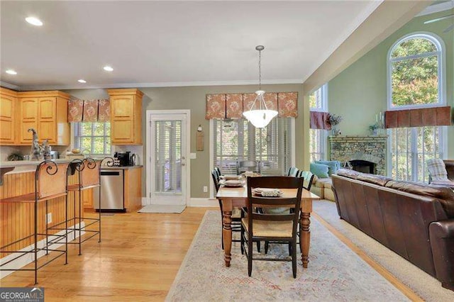 dining room with baseboards, light wood-style flooring, recessed lighting, a stone fireplace, and crown molding