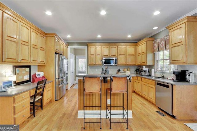 kitchen with a sink, stainless steel appliances, a kitchen island, and light wood finished floors