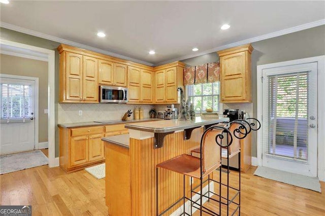 kitchen featuring light wood-type flooring, stainless steel microwave, a kitchen bar, and backsplash