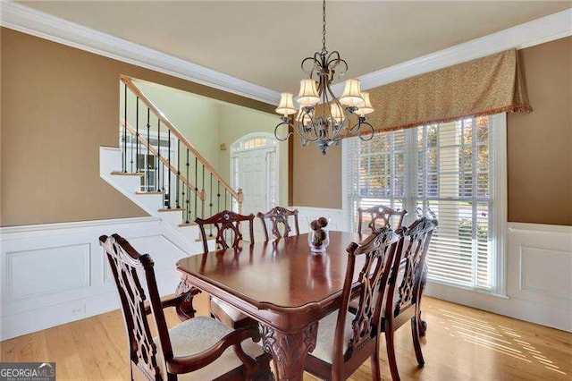 dining room featuring an inviting chandelier, a wainscoted wall, light wood finished floors, and ornamental molding