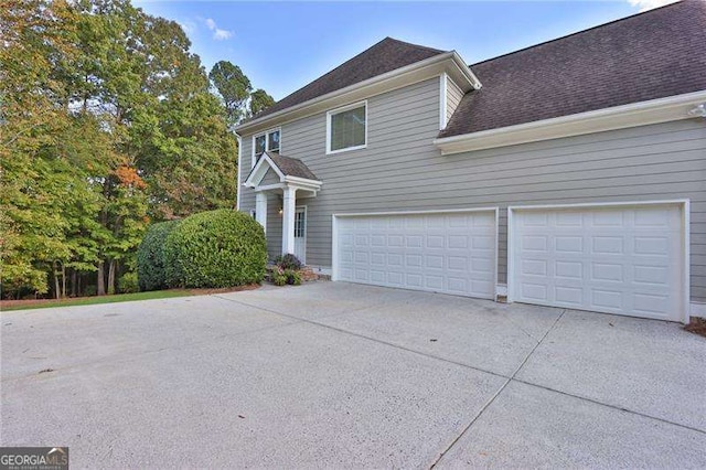 view of side of home with a garage, driveway, and a shingled roof