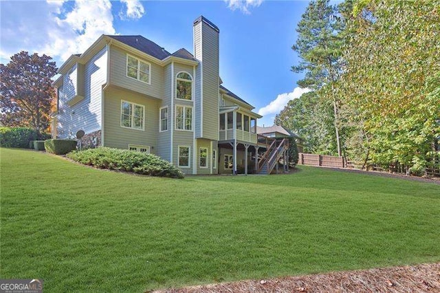 rear view of house featuring stairway, a lawn, a chimney, and a sunroom