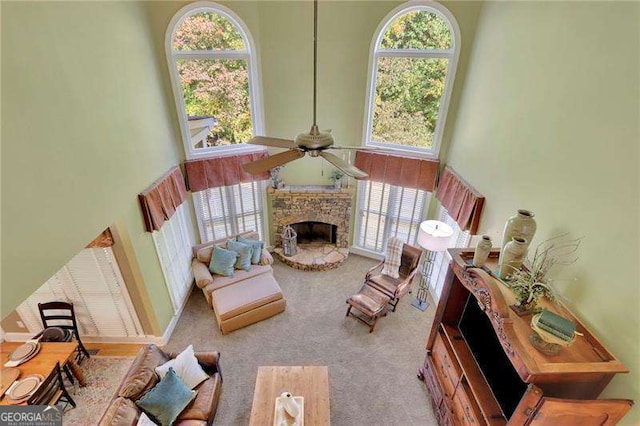 living room with a ceiling fan, a stone fireplace, a high ceiling, and carpet