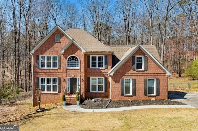 view of front of home featuring brick siding, a shingled roof, a front lawn, and fence