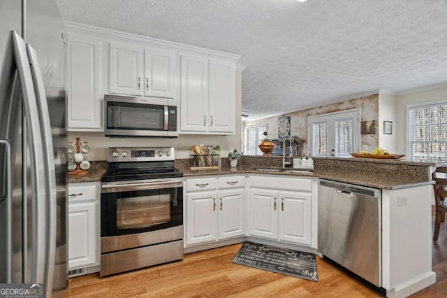 kitchen featuring a peninsula, a sink, white cabinets, appliances with stainless steel finishes, and light wood-type flooring