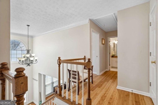 hall featuring baseboards, attic access, a textured ceiling, an upstairs landing, and light wood-type flooring