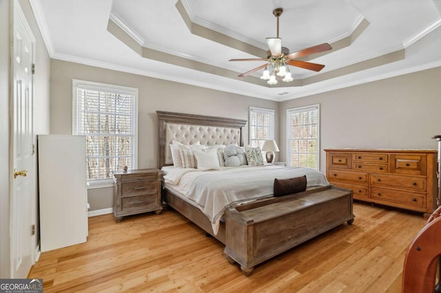 bedroom with multiple windows, light wood-type flooring, and a raised ceiling