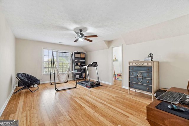 exercise room with a ceiling fan, baseboards, lofted ceiling, light wood-style flooring, and a textured ceiling