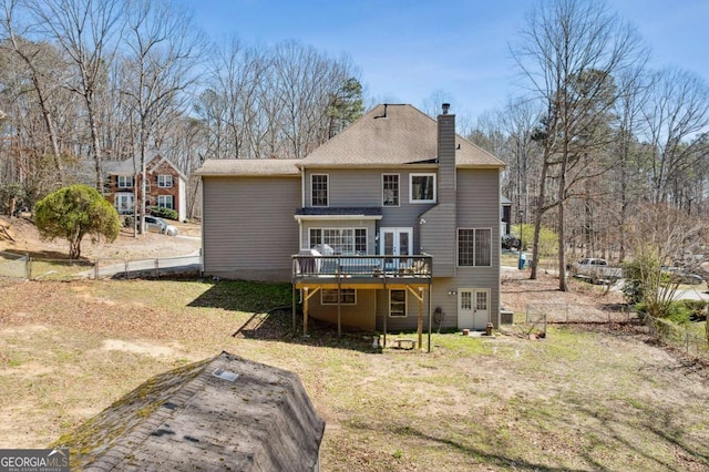 rear view of property with fence, a wooden deck, roof with shingles, a lawn, and a chimney