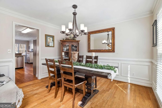 dining area featuring a chandelier, light wood-style flooring, wainscoting, and ornamental molding