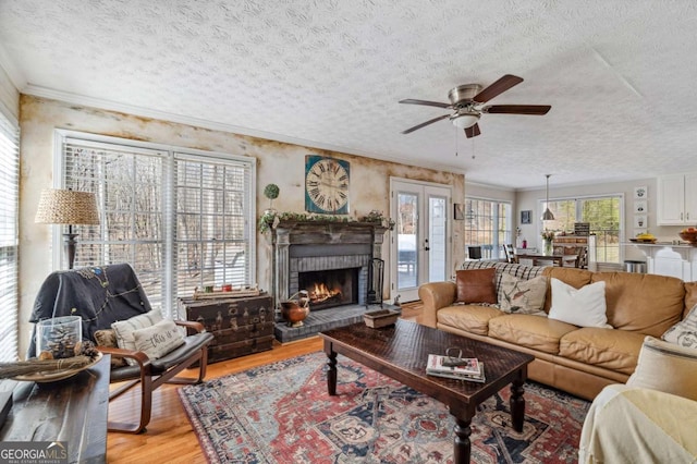 living area with light wood-type flooring, a ceiling fan, a textured ceiling, crown molding, and a brick fireplace