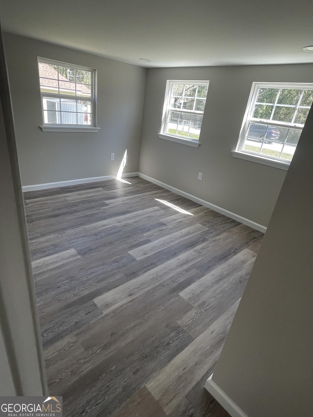 spare room with dark wood-type flooring, a healthy amount of sunlight, and baseboards