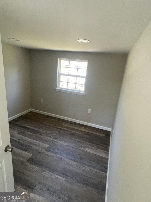 empty room featuring baseboards and dark wood-type flooring