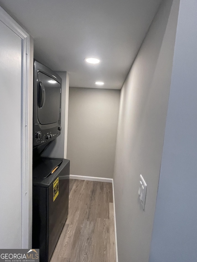 washroom with baseboards, wood finished floors, laundry area, and stacked washer / dryer