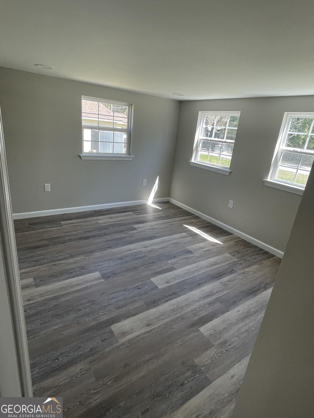 spare room with baseboards, plenty of natural light, and dark wood-type flooring