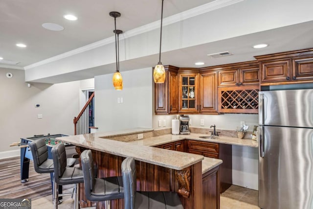 kitchen with crown molding, light stone countertops, a peninsula, freestanding refrigerator, and a sink