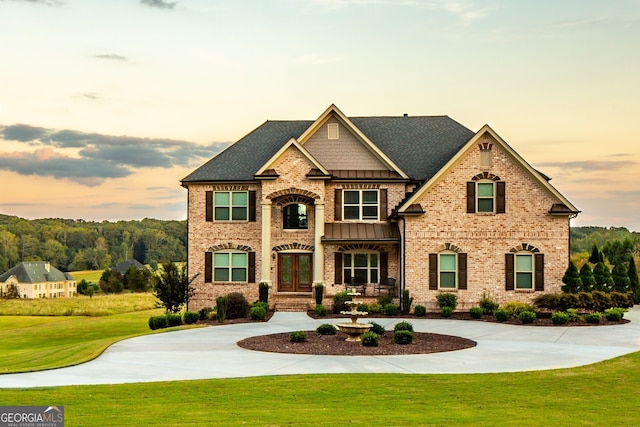 view of front of house featuring a lawn, french doors, brick siding, and curved driveway