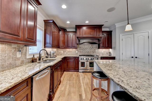kitchen featuring a kitchen bar, light stone countertops, a sink, stainless steel appliances, and light wood-style flooring