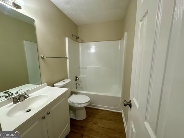 full bath with toilet, a textured ceiling, shower / washtub combination, wood finished floors, and vanity