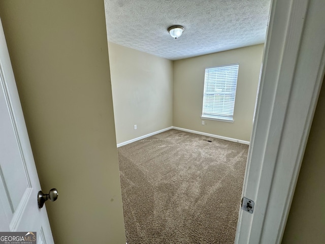 empty room with carpet flooring, baseboards, and a textured ceiling