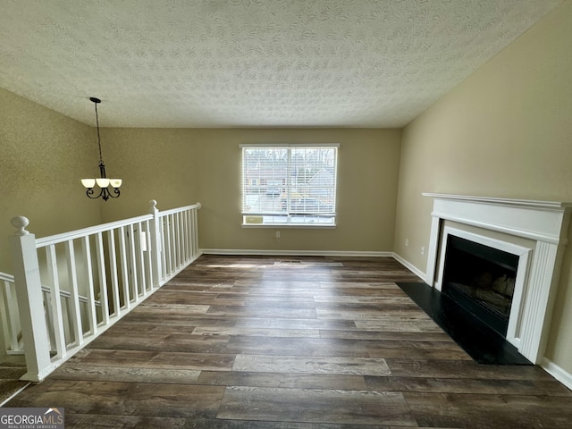 unfurnished living room featuring wood finished floors, baseboards, an inviting chandelier, a fireplace with flush hearth, and a textured ceiling