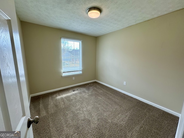 empty room with baseboards, visible vents, dark carpet, and a textured ceiling