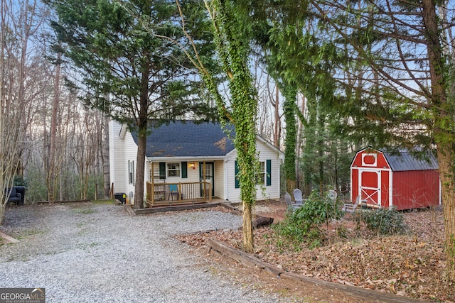 view of front of property featuring a barn, gravel driveway, a porch, roof with shingles, and an outdoor structure