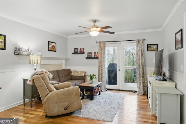 living area featuring a ceiling fan, hardwood / wood-style floors, french doors, wainscoting, and crown molding