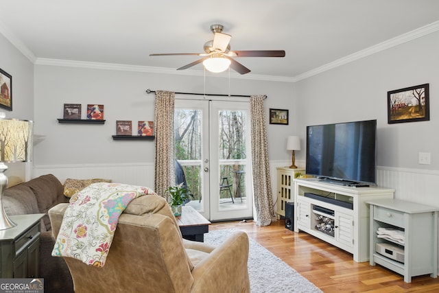 living area with light wood-style floors, a wainscoted wall, french doors, and ornamental molding