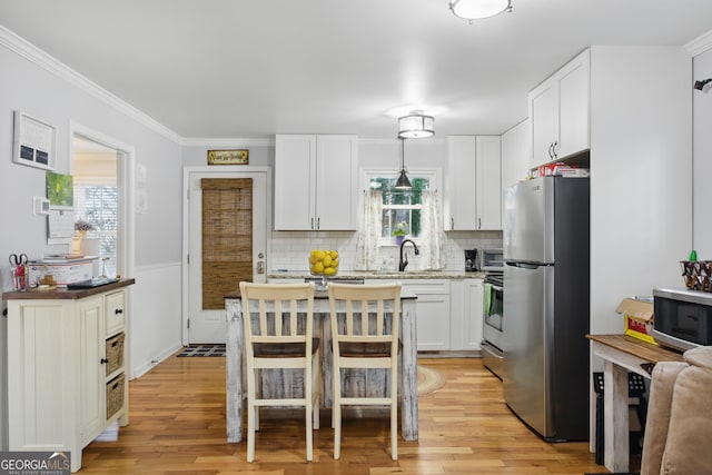 kitchen with light wood finished floors, appliances with stainless steel finishes, a healthy amount of sunlight, and white cabinetry