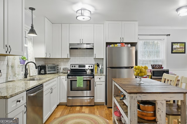 kitchen featuring under cabinet range hood, ornamental molding, white cabinets, stainless steel appliances, and a sink