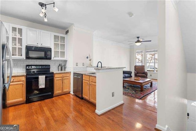 kitchen with wood finished floors, a peninsula, a sink, black appliances, and backsplash