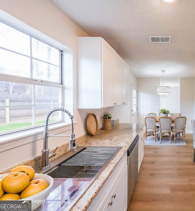 kitchen featuring visible vents, decorative light fixtures, light wood-style flooring, white cabinets, and stainless steel dishwasher