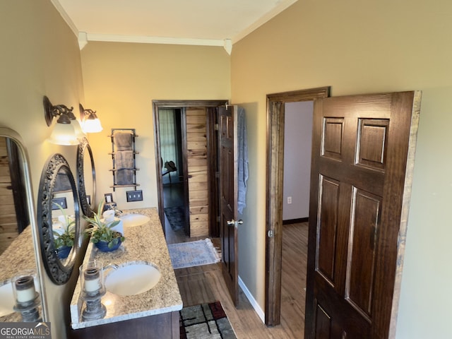 full bathroom with wood finished floors, baseboards, double vanity, ornamental molding, and a sink