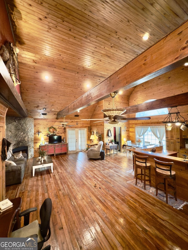 living area featuring wood-type flooring, a stone fireplace, wood walls, wood ceiling, and vaulted ceiling with beams