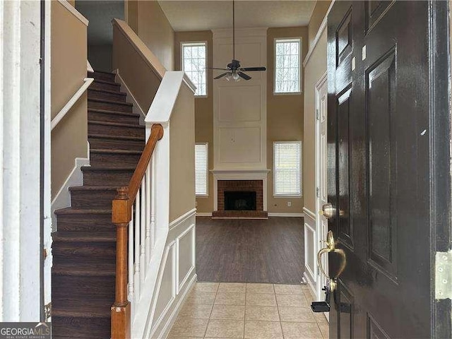 tiled foyer featuring a ceiling fan, baseboards, a high ceiling, stairs, and a brick fireplace